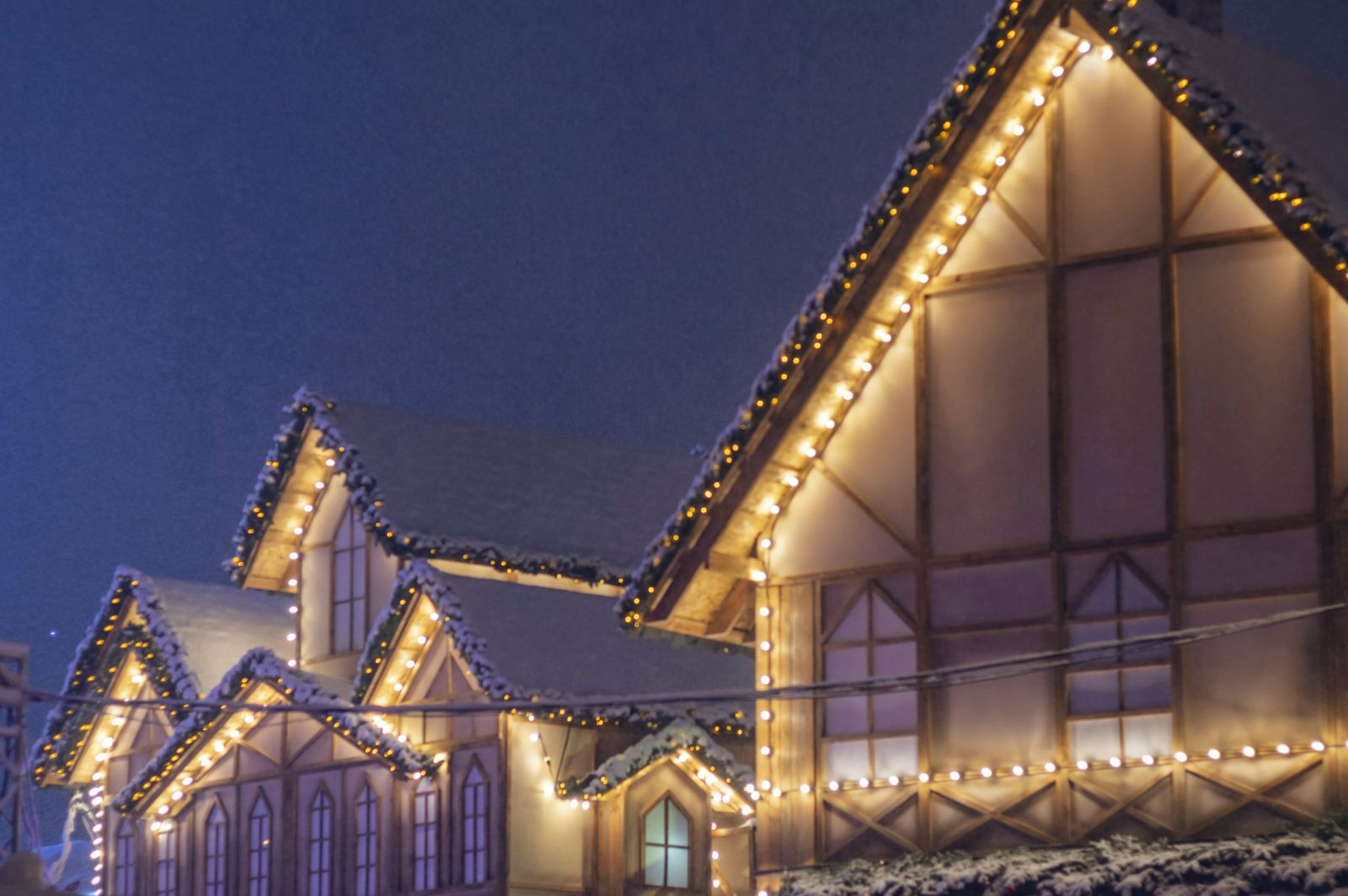 Steep gables outlined in warm white bulbs against a deep blue night sky