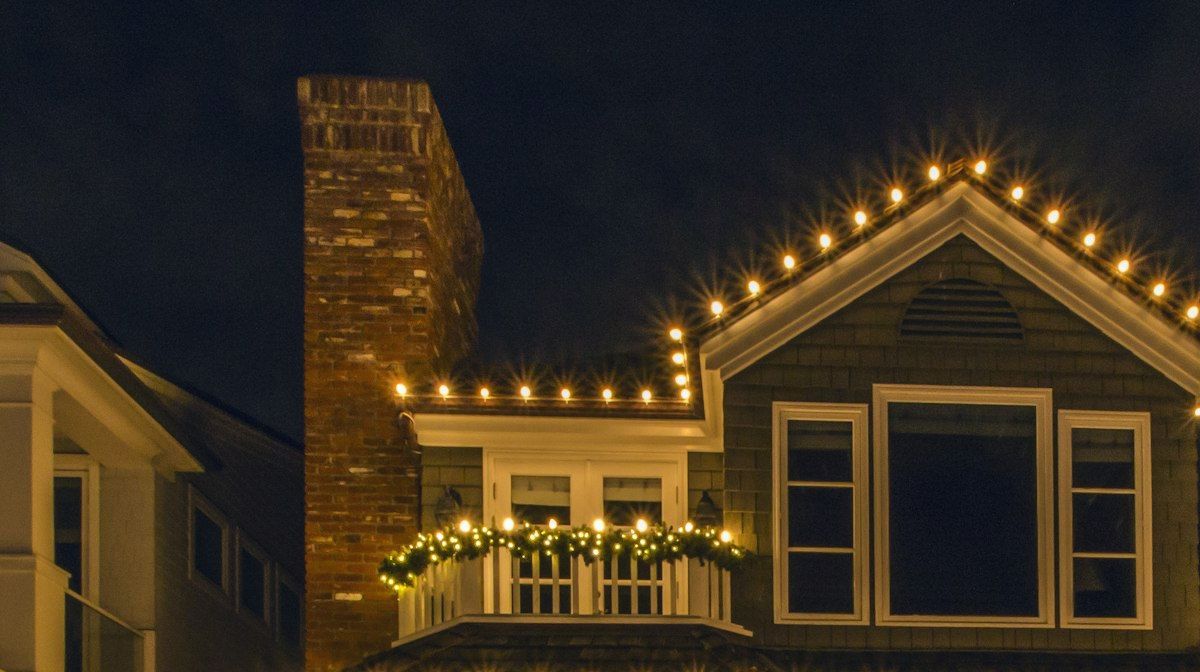 Roof peak and chimney outlined in warm white bulbs, with garland on the balcony below