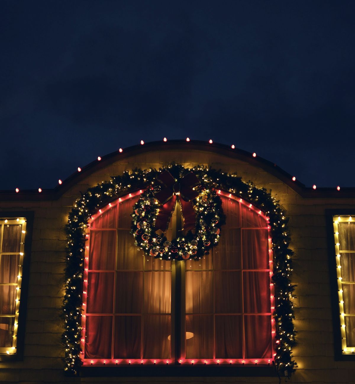 Large lit wreath hung in an arched window framed with garland